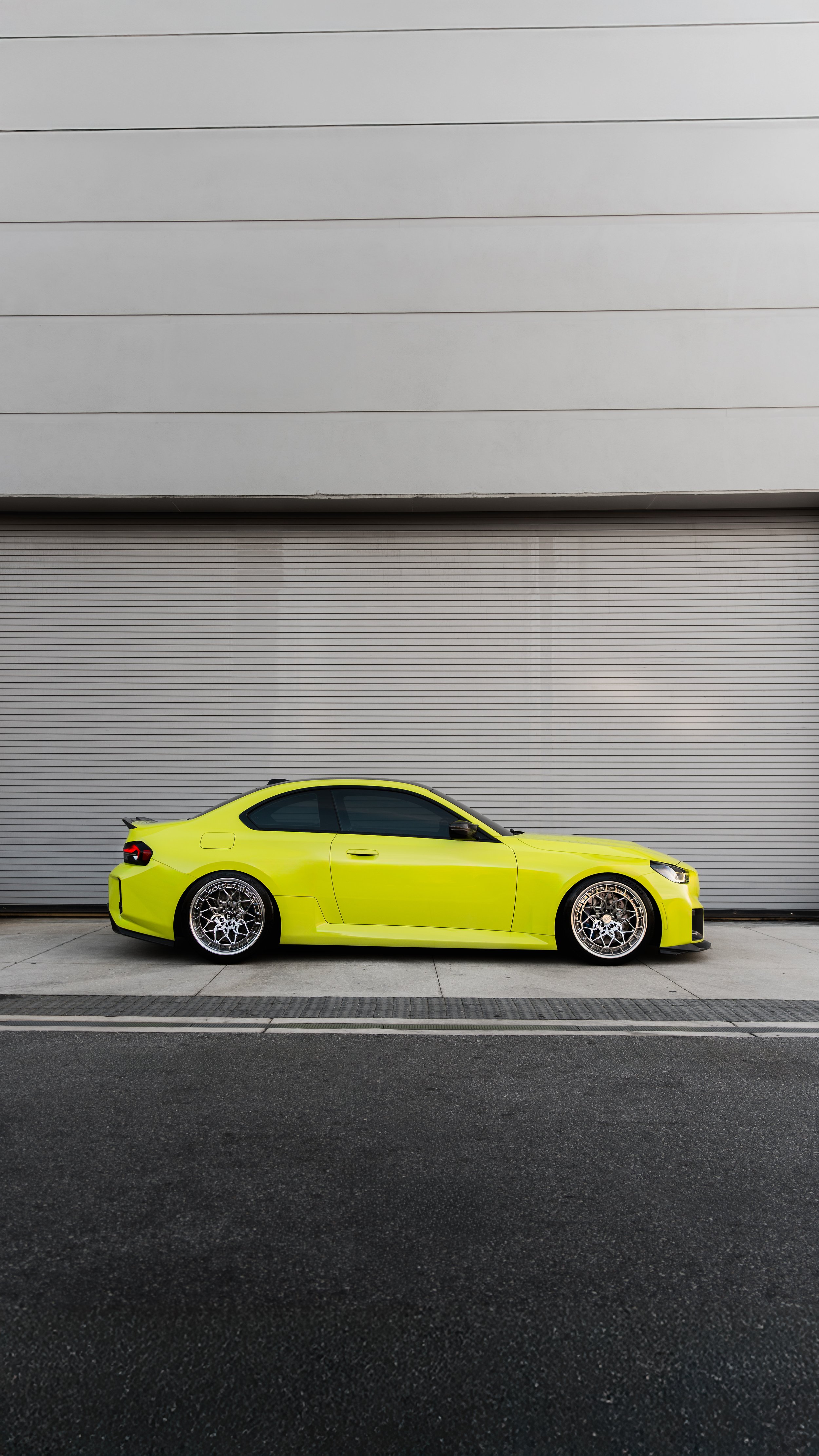 A yellow sports car parked in front of a gray industrial building with a large rolling door