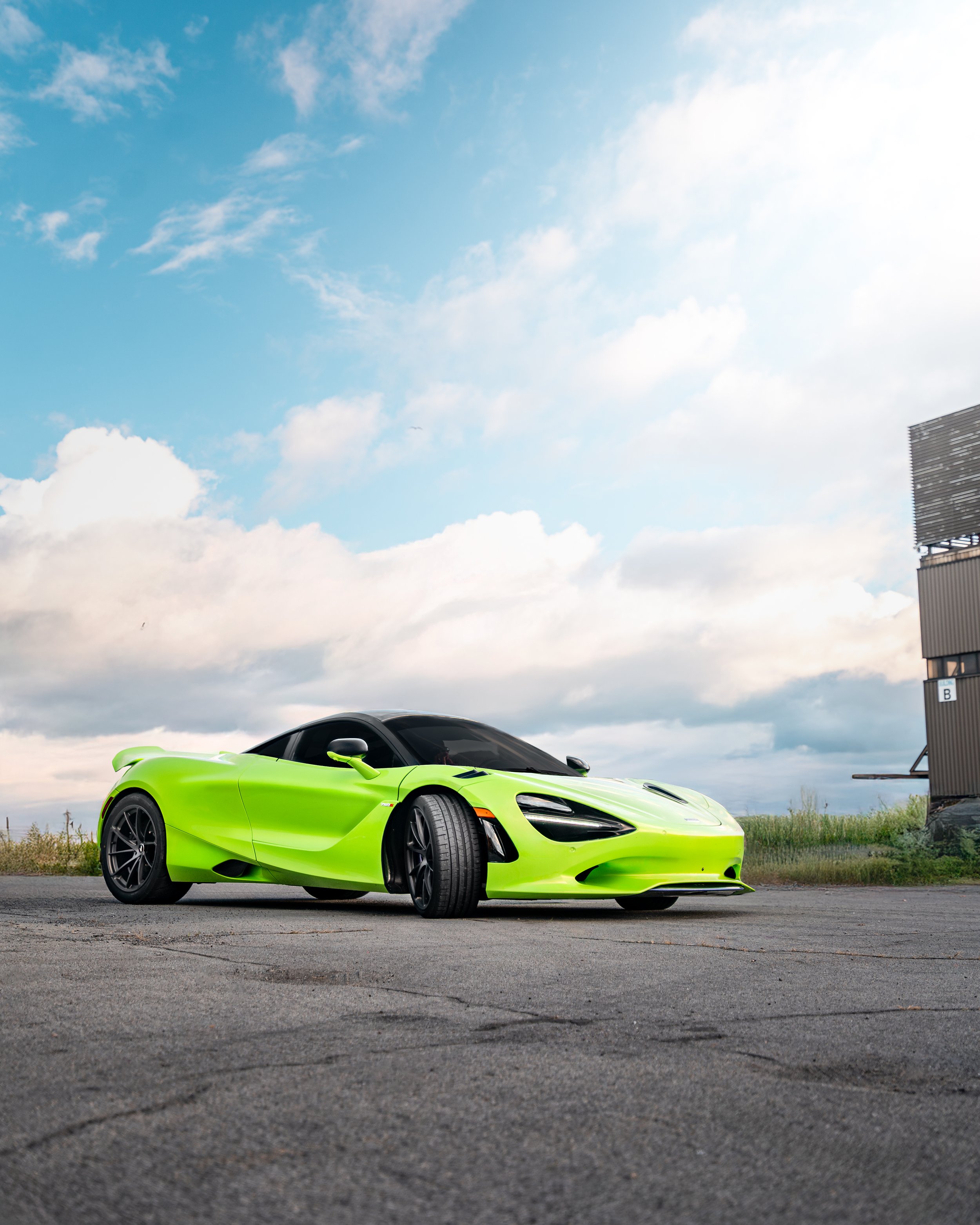 A bright green Mclaren 750s parked on an empty asphalt lot with a cloudy sky in the background.