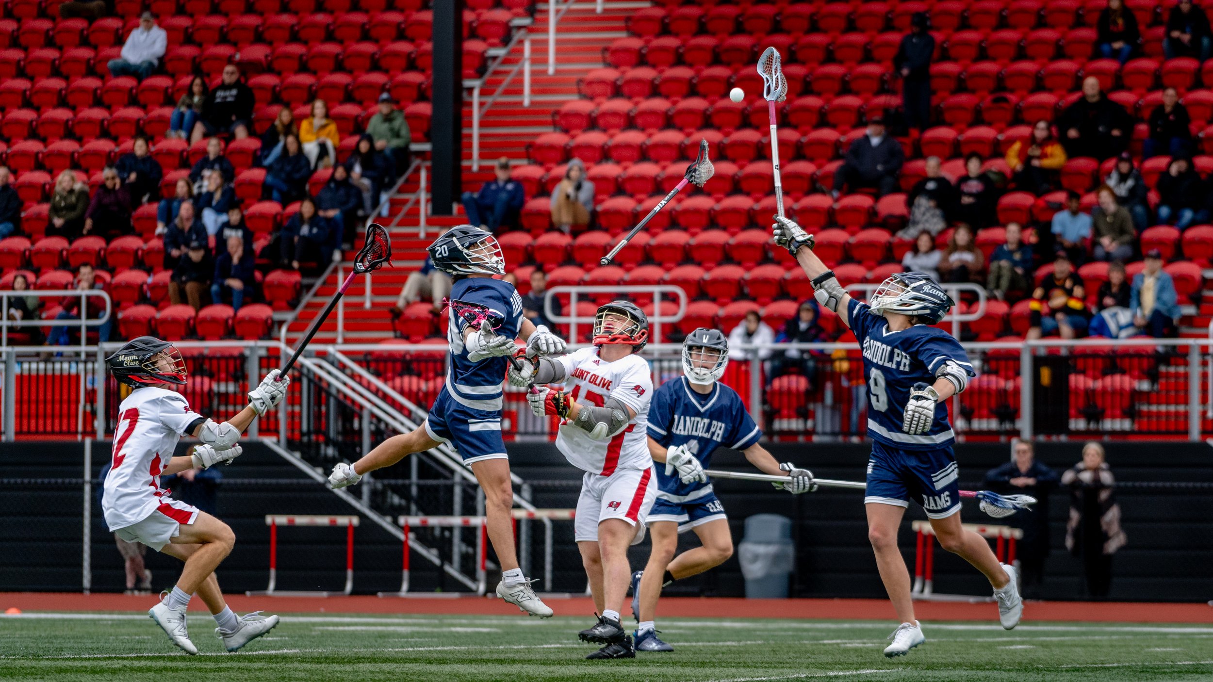 Lacrosse players in action on field with spectators in stands
