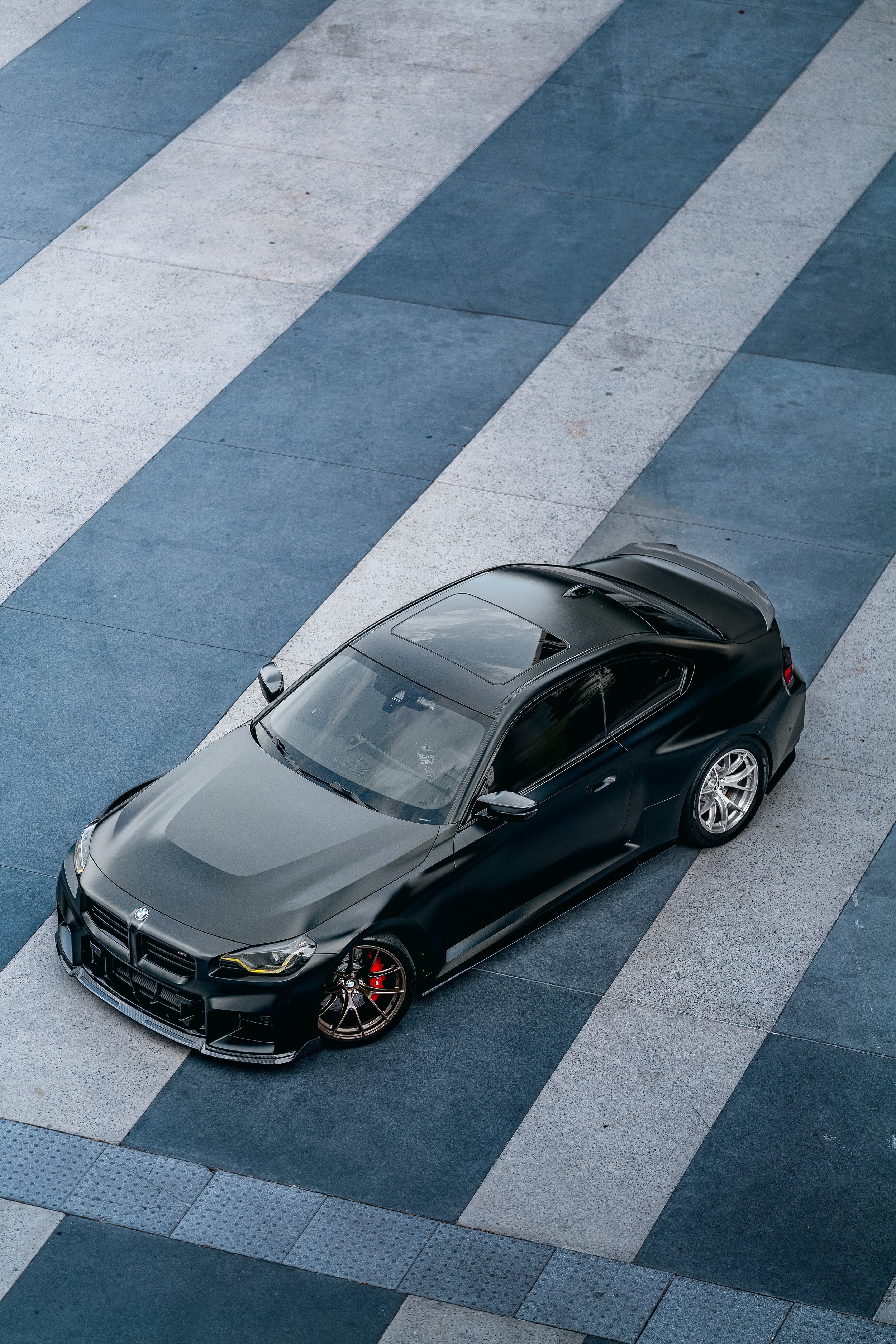 A black BMW M2 parked on a concrete surface with alternating light and dark gray tiles in Orlando, Florida